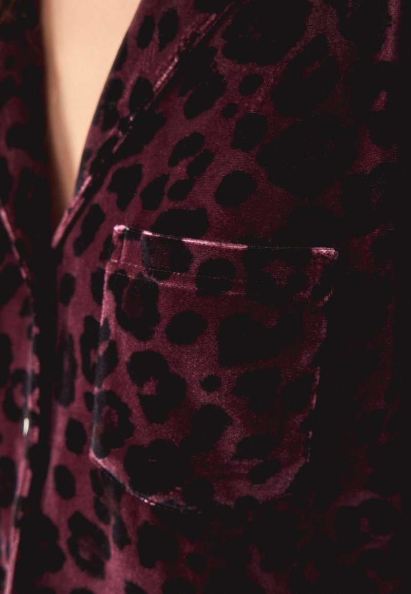 Camisa de pijama de terciopelo en burdeos con estampado de leopardo negro. Cuenta con un bolsillo en el pecho y una textura similar a la seda.