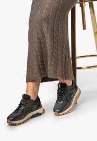Baskets de sport noires et texturées avec une semelle en caoutchouc gomme, présentant des matériaux contrastés et des coutures détaillées.