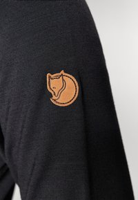 Svetario nero con un'emblema di volpe in pelle marrone sulla manica, con una texture liscia e un design aderente.