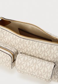 Μπεζ υφασμάτινο πουγκί με χρυστό φερμουάρ, με υφή μοτίβου από διαπλεκόμενα γράμματα. Περιέχει δύο μικρότερες θήκες με φερμουάρ.