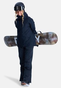Snowboardzista w granatowej kurtce i spodniach, trzymający deskę snowboardową w wzory. Ma na sobie czarny kask i gogle, z teksturowanymi detalami na materiale.