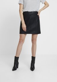 Svart faux läder A-linje kjol med subtil textur, med hög midja och vertikala sömdetaljer, som matchas med svarta ankelstövlar.