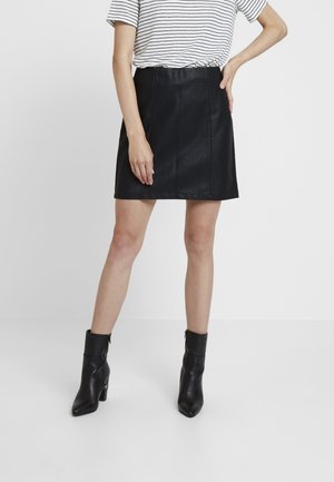 Jupe A-line en simili cuir noir avec une texture subtile, dotée d'une taille haute et de détails de couture verticaux, associée à des bottines noires.