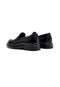 Mocasines de cuero negro brillante con tacones bajos apilados y pequeños tachuelas plateadas alrededor del borde de la suela, vistos desde la parte trasera y lateral.