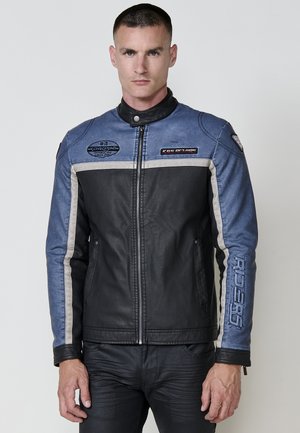 Chaqueta de moto de mezclilla azul y cuero negro. Presenta un cuello alto, cremallera frontal y rayas en gris claro contrastantes. Logotipos en el pecho.
