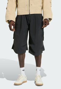 Black, knee-length cargo shorts with pleats, lightweight fabric, side pockets, paired with white mid-calf socks and cream sneakers.