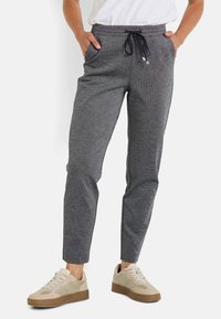Pantalon de jogging en tricot gris avec taille à cordon, deux poches latérales et design de jambe fuselée, associé à des baskets beige.