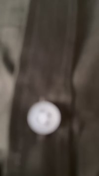 Un pulsante su un tessuto scuro e strutturato con cuciture visibili. Il pulsante è bianco con un design circolare e quattro fori per l'attacco.