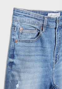 Jeans de mezclilla azul claro con un talle medio, dos bolsillos frontales y un sutil desgaste. Los remaches de cobre y los detalles de costura realzan el diseño.