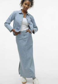 Črtasta jeans jakna z gumbi in žepi, v kombinaciji z usklajeno dolgo krilo z bočnim razporkom. Obuta z belimi supergami.