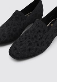 Zapatos negros sin cordones con un patrón texturizado a cuadros. Hechos de material transpirable, con una puntera redondeada y un diseño minimalista.