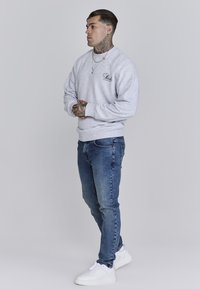 Grauer Sweatshirt mit gerippten Bündchen und Saum, kombiniert mit blauen Jeans. Weiße Sneakers runden das Outfit ab und sorgen für einen lässigen Look.