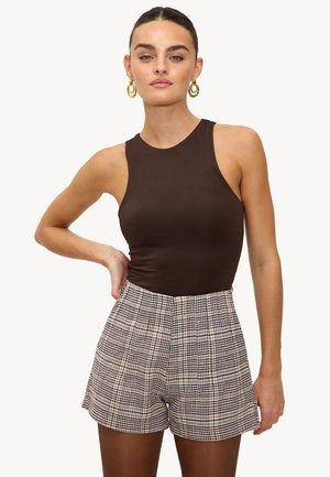 Bruine geribbelde bodysuit gecombineerd met hoge, geplaid shorts in beige, bruin en blauwe tinten. Gouden oorbellen in de vorm van een ring accentueren de look.