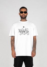 Balta medvilninė t-shirt marškiniai su juodu grafiniu spausdinimu, ant kurio užrašyta "MOAE JUZS". Marškiniai turi trumpas rankoves ir laisvą fasoną.