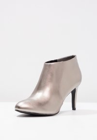 Botín metálico plateado con puntera puntiaguda, textura lisa y un tacón alto y delgado. Presenta un diseño sin costuras y una silueta minimalista.