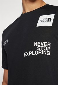Svart bomulls t-skjorte med korte ermer, rund hals og hvit grafisk tekst: "THE NORTH FACE" og "NEVER STOP EXPLORING."