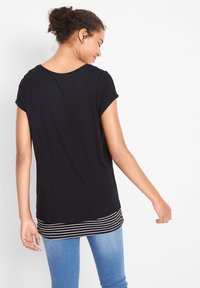 T-shirt noir à manches courtes avec un col rond et un ourlet rayé. Le tissu semble doux avec une texture lisse, s'ajustant de manière lâche.