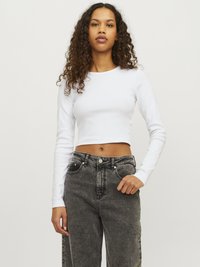 Top corto bianco a maniche lunghe con collo rotondo, abbinato a jeans a gamba larga neri sbiaditi a vita alta con tasche frontali e accessori in metallo.
