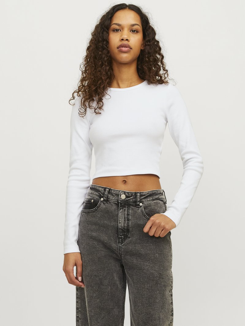 Top corto bianco a maniche lunghe con collo rotondo, abbinato a jeans a gamba larga neri sbiaditi a vita alta con tasche frontali e accessori in metallo.