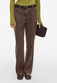 Hnědé džíny s vysokým pasem vyrobené z denimu, s rovným střihem, bočními kapsami a tmavohnědým opaskem. V kombinaci s tmavohnědými botami.