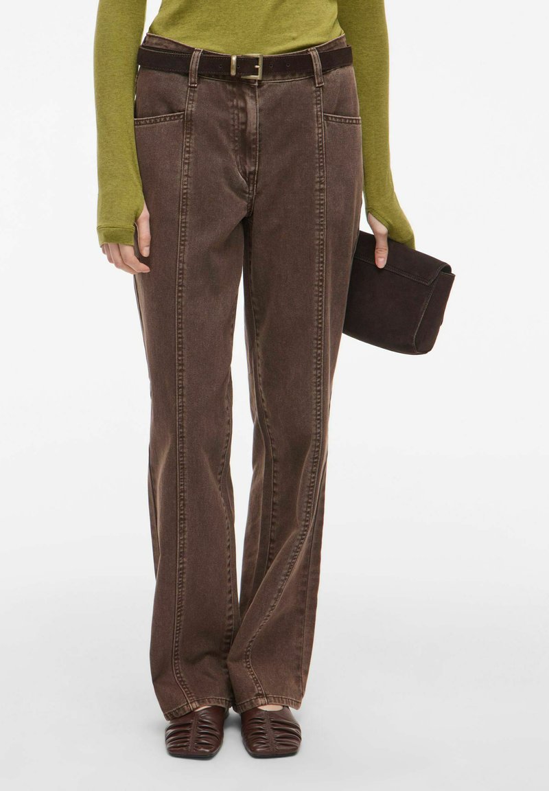 Hnědé džíny s vysokým pasem vyrobené z denimu, s rovným střihem, bočními kapsami a tmavohnědým opaskem. V kombinaci s tmavohnědými botami.