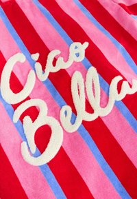 Kolorowa tkanina z pionowymi paskami w kolorach czerwonym, różowym i niebieskim, z fakturowanym białym pisanym napisem „Ciao Bella”.