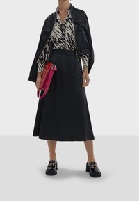 Black satin bomber jacket over a patterned blouse, paired with a black midi skirt. Holding a pink handbag. Black chunky shoes with hardware.