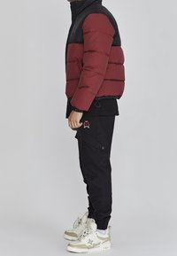 Dunjakke med sort øvre del og bordeaux nederste del, kombineret med sorte cargobukser og beige sneakers med hvide detaljer.