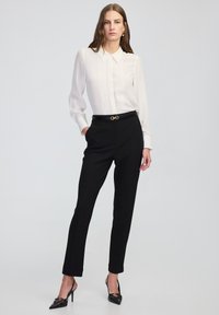 Bílá blůza s sklady, černé kalhoty na míru, černý opasek se zlatými detaily a černé špičaté lodičky. Hladká tkanina a obepínající střih.