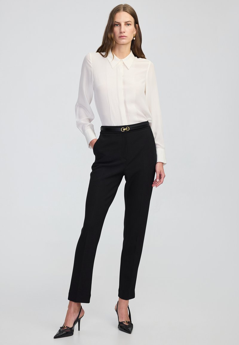 Bílá blůza s sklady, černé kalhoty na míru, černý opasek se zlatými detaily a černé špičaté lodičky. Hladká tkanina a obepínající střih.