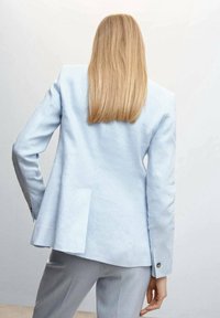 Blazer en lin bleu clair avec une coupe ajustée, une fente simple au dos et des poignets boutonnés. Texture lisse avec des détails minimaux.