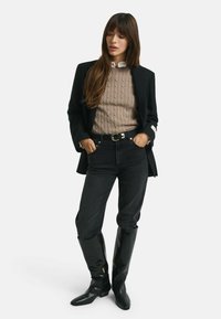 Zwarte op maat gemaakte blazer over een beige kabelgebreide trui, gecombineerd met hoge zwarte jeans en kniehoge zwarte leren laarzen.