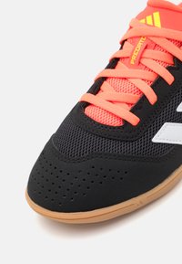 Czarne buty sportowe z siateczkową cholewką, pomarańczowymi sznurowadłami i białym logo. Posiada perforowaną strukturę oraz podeszwę z gumy, zapewniającą przyczepność.