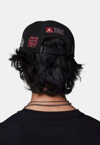 Cappello nero con dettagli ricamati, tra cui "23" e "Brand of Flight", dotato di chiusura snapback e tessuto testurizzato.