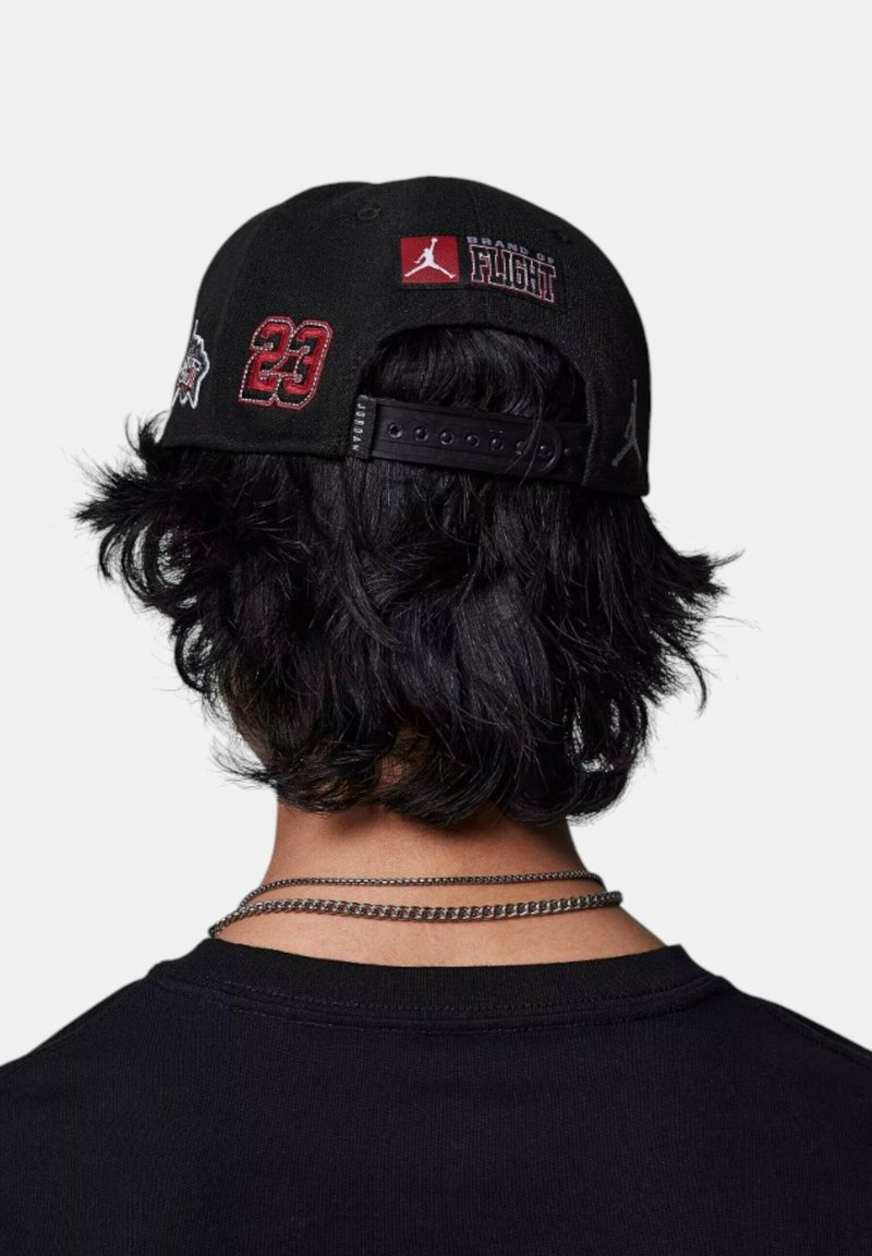 Cappello nero con dettagli ricamati, tra cui "23" e "Brand of Flight", dotato di chiusura snapback e tessuto testurizzato.