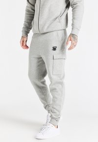 Szare spodnie dresowe o slim fit, z bocznymi kieszeniami i kieszenią na cargo. Posiadają małe czarne logo na lewej udzie. W zestawie z białymi sneakersami.