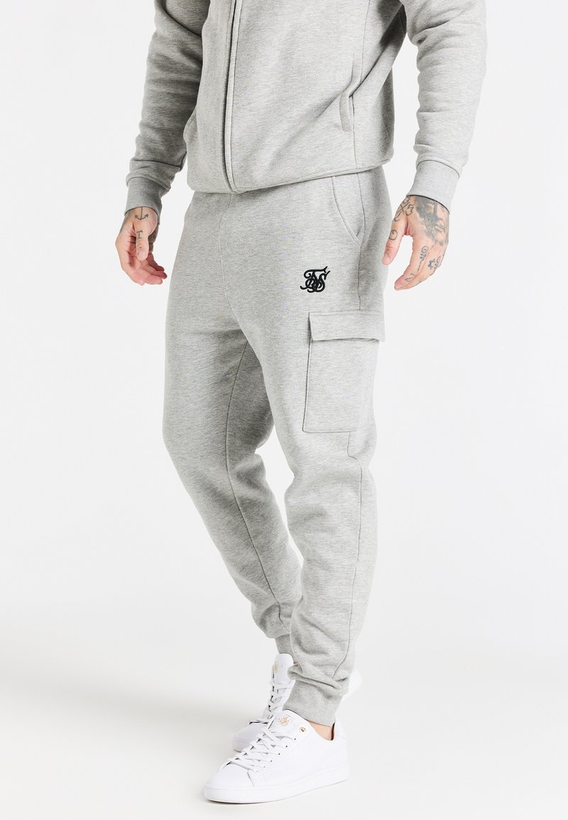 Szare spodnie dresowe o slim fit, z bocznymi kieszeniami i kieszenią na cargo. Posiadają małe czarne logo na lewej udzie. W zestawie z białymi sneakersami.