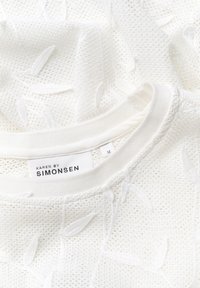 Valge kudum, millel on lehekujuliste mustrite tekstuur, ribaga kaelus ja silt "Karen by Simonsen", suurus M.