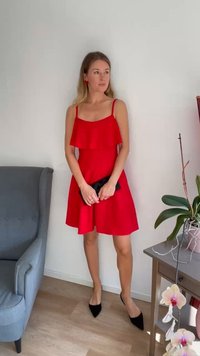 Röd ärmlös klänning med lager av volanger, figurnära liv och utsvängd kjol, kombinerad med svart kuvertväska och spetsiga svarta klackar.