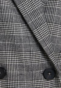 Dwurzędowy żakiet w czarno-białą kratę houndstooth, z teksturowanej tkaniny i dużymi czarnymi guzikami.