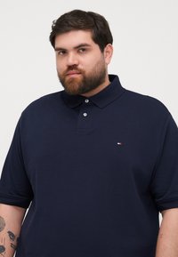 Marineblauw poloshirt met korte mouwen, gemaakt van een katoenmix, met een twee-knopenlijst en een klein logo op de linkerborst.