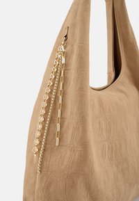 Beigefarbene Wildleder-Umhängetasche mit strukturierter Oberfläche, verziert mit goldenen Kettenakzenten und einem kontrastierenden glatten Bereich. Weiches, geräumiges Design.