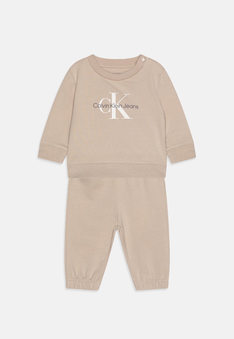 Beżowy komplet z bawełny składający się z bluzki z okrągłym dekoltem z logo "Calvin Klein Jeans" oraz dopasowanych spodni z elastycznym pasem i mankietami na kostkach.