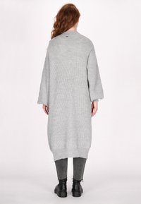 Lange, loszittende grijze gebreide trui met een textuurpatroon, drop sleeves en een ronde halslijn, gecombineerd met donkere grijze skinny broeken en zwarte laarzen.