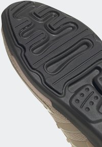 Rubber sneaker sole in black with textured grip patterns. Light brown synthetic upper with horizontal stripes and minimal hardware accents.