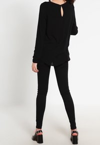 Haut noir à manches longues avec un détail d'ouverture dans le dos, associé à un jean skinny noir et des sandales à talons noires avec des brides autour de la cheville.