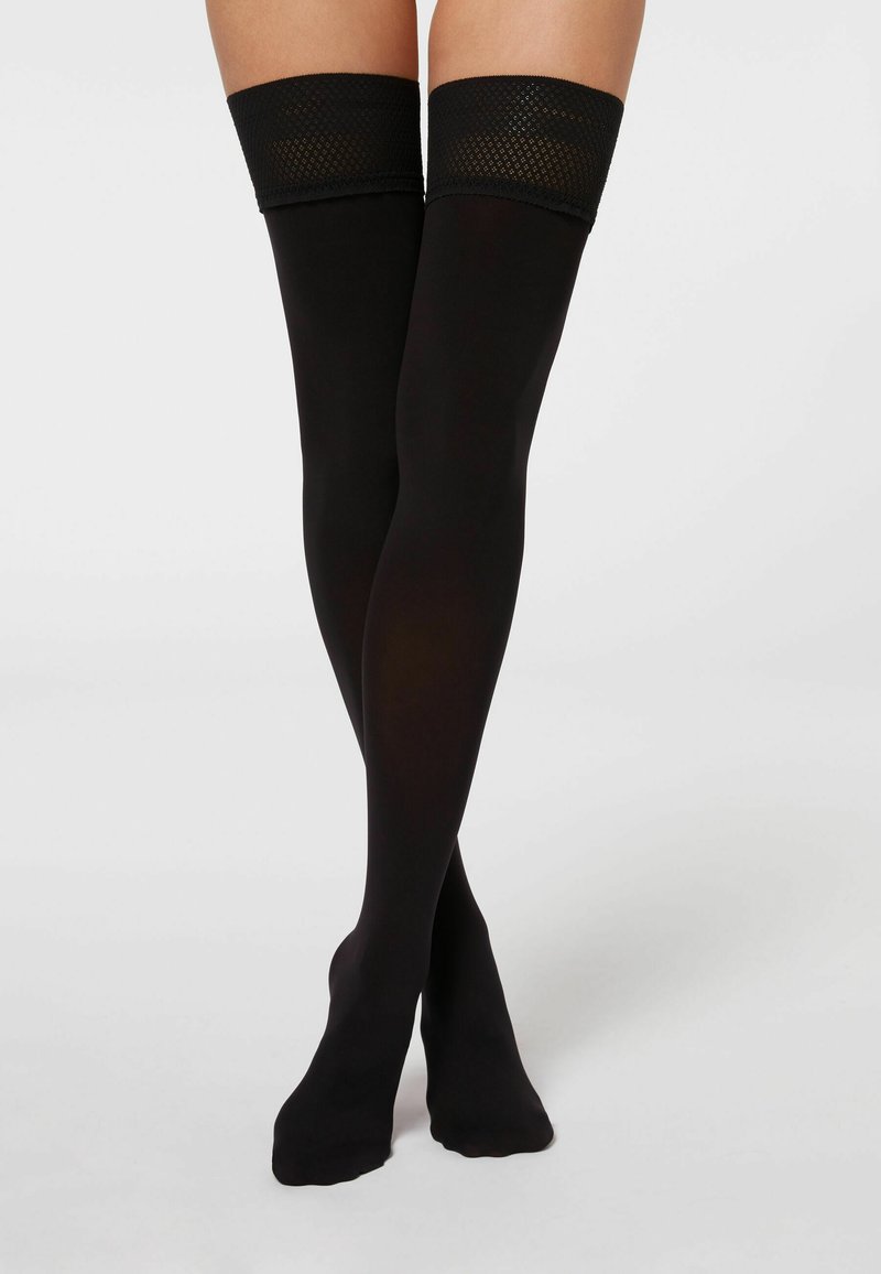 Sorte thigh-high strømper med en gennemsigtig finish, der har et tekstureret fiskenetbånd øverst. Glat tekstur og tætsiddende design.
