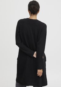 Schwarze Strickjacke mit langen Ärmeln und entspannter Passform, ausgestattet mit Seitentaschen und einer strukturierten Oberfläche.