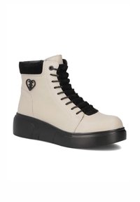 Białe wysokie buty z czarnymi zamszowymi akcentami, z przodu sznurowane, z gumową podeszwą i detalem w kształcie serca po boku.