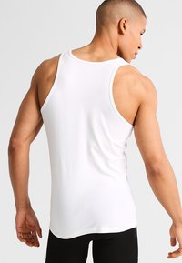 Biały bawełniany top na ramiączkach z okrągłym dekoltem i szerokimi ramiączkami, prezentujący dopasowany krój oraz gładką teksturę z widoku z tyłu.